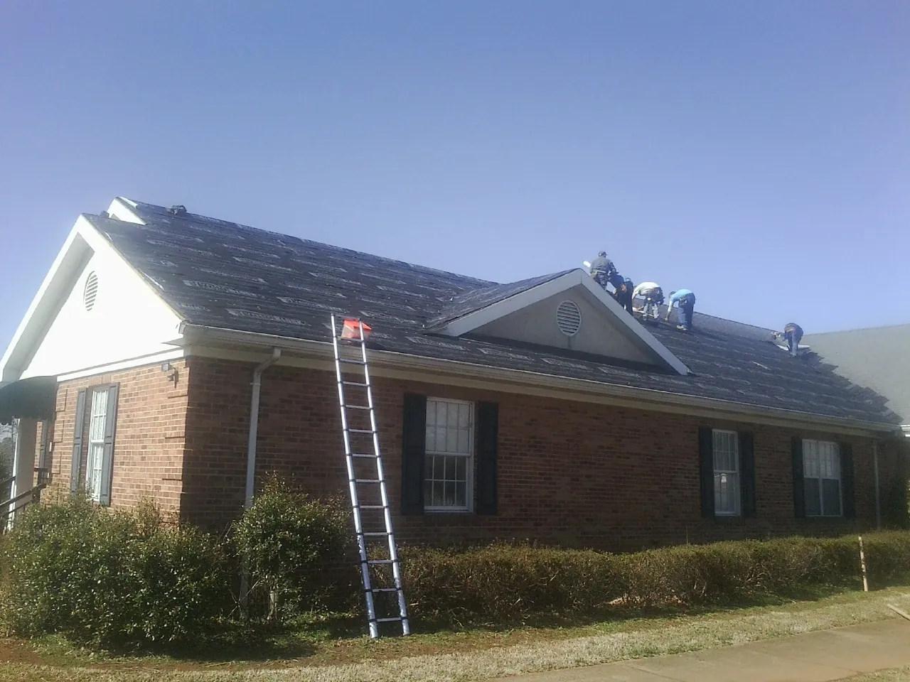 Crew tearing shingles off a brick ranch roof with a ladder set — Metal Roof Repair work by our crew in Shipshewana
