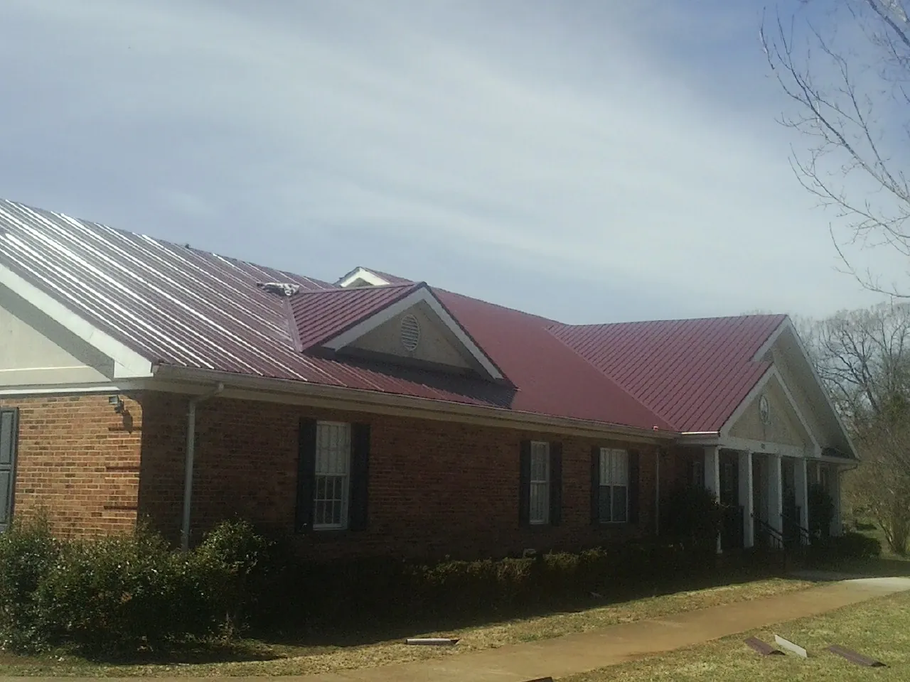 Red metal roof with gabled entries on a long brick building, from a Hail Damage Roof Repair job in Shipshewana