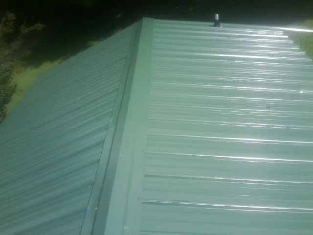 New green metal panels meeting at the ridge of a roof — Flat Roof Repair work by our crew in Shipshewana