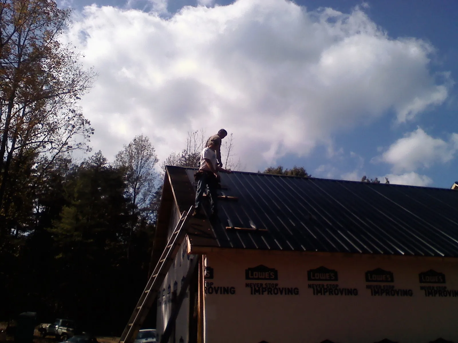 Roofer fastening dark metal panels high against a cloudy sky, from a Roof Inspection job in Shipshewana