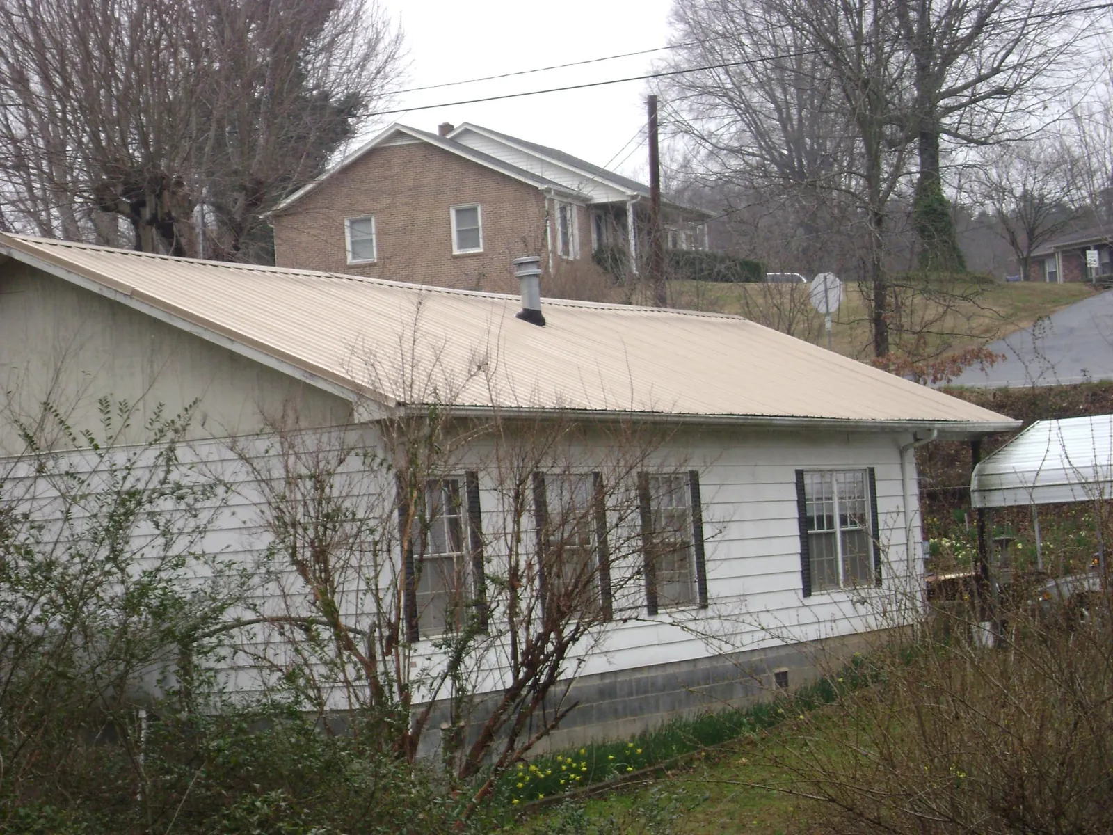 Tan metal roof on a white sided house set into a hillside — Commercial Roofing by Roofing Brothers in Shipshewana